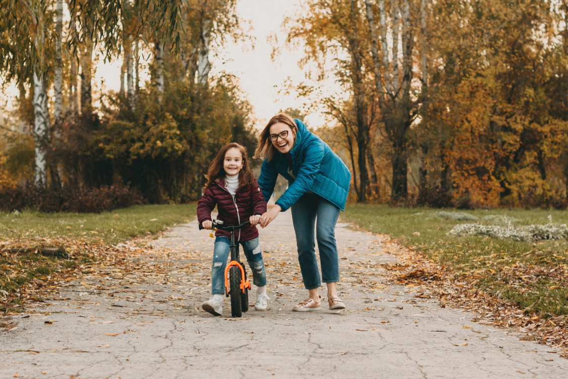 Lachende Frau hilft Kind beim Laufrad fahren