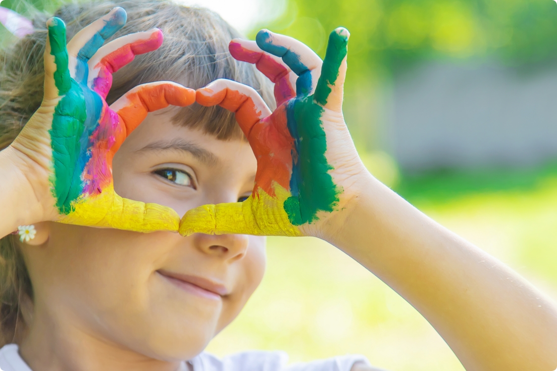 Kind mit angemalten Fingern lacht in die Kamera
